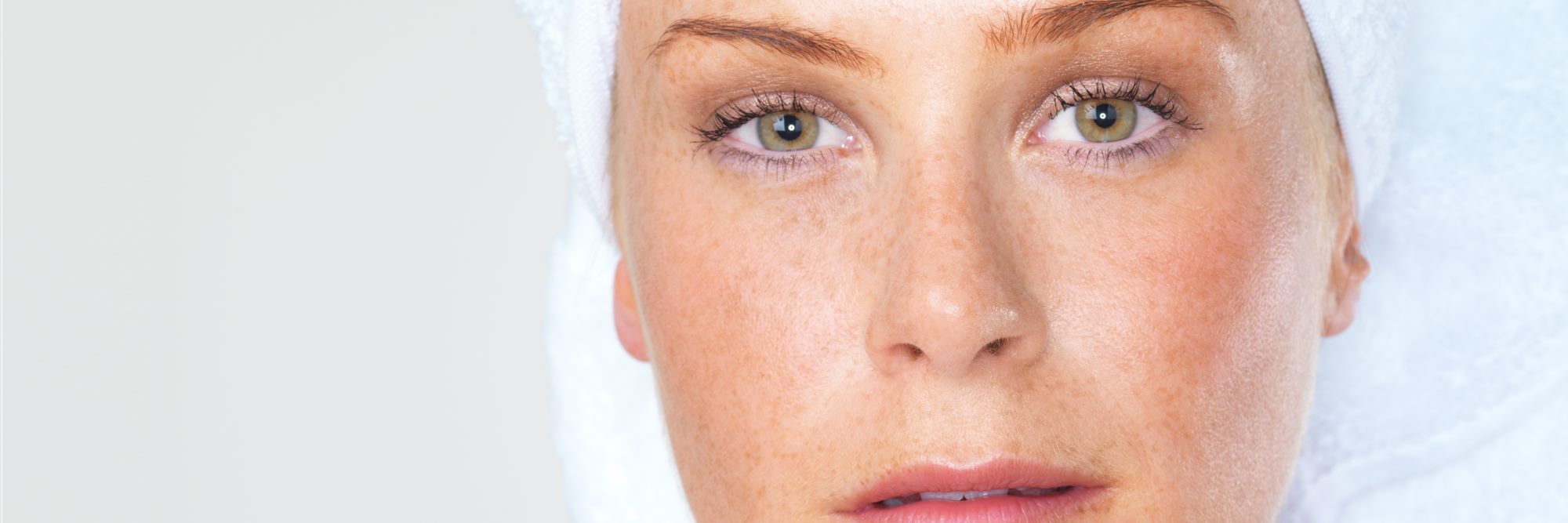 A close view of a woman's face, her hair wrapped in a white towel, her freckled skin evenly lit.